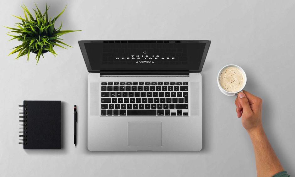 Minimalist workspace with a laptop, notebook, and coffee cup on a grey desk.